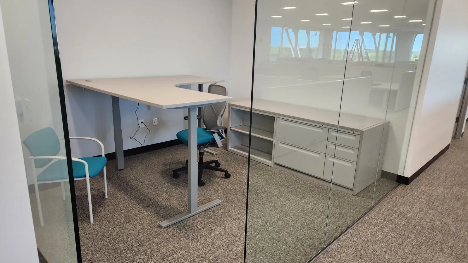 Height-adjustable corner workstation fitted against a glass office wall
