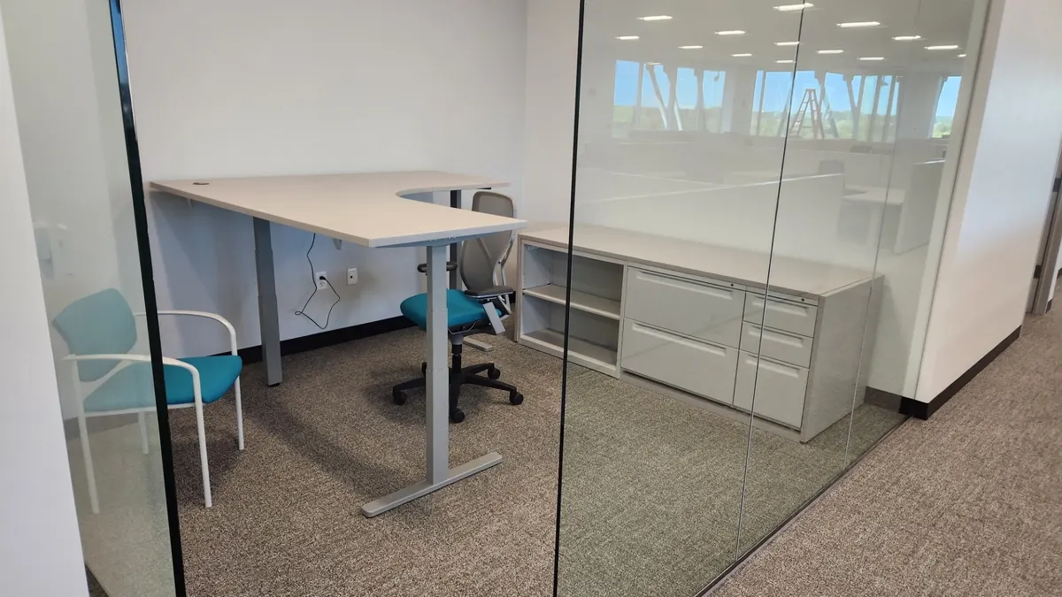 Corner sit-stand desk built against a glass office wall